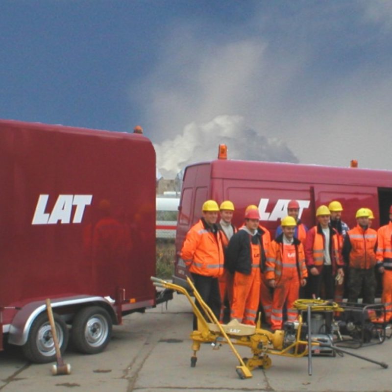 Geschichte der LAT-Gruppe - LAT Mitarbeiter posieren vor LAT Dienstwagen, ICE der Deutschen Bahn im Hintergrund.